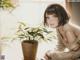 A woman sitting at a table next to a potted plant.